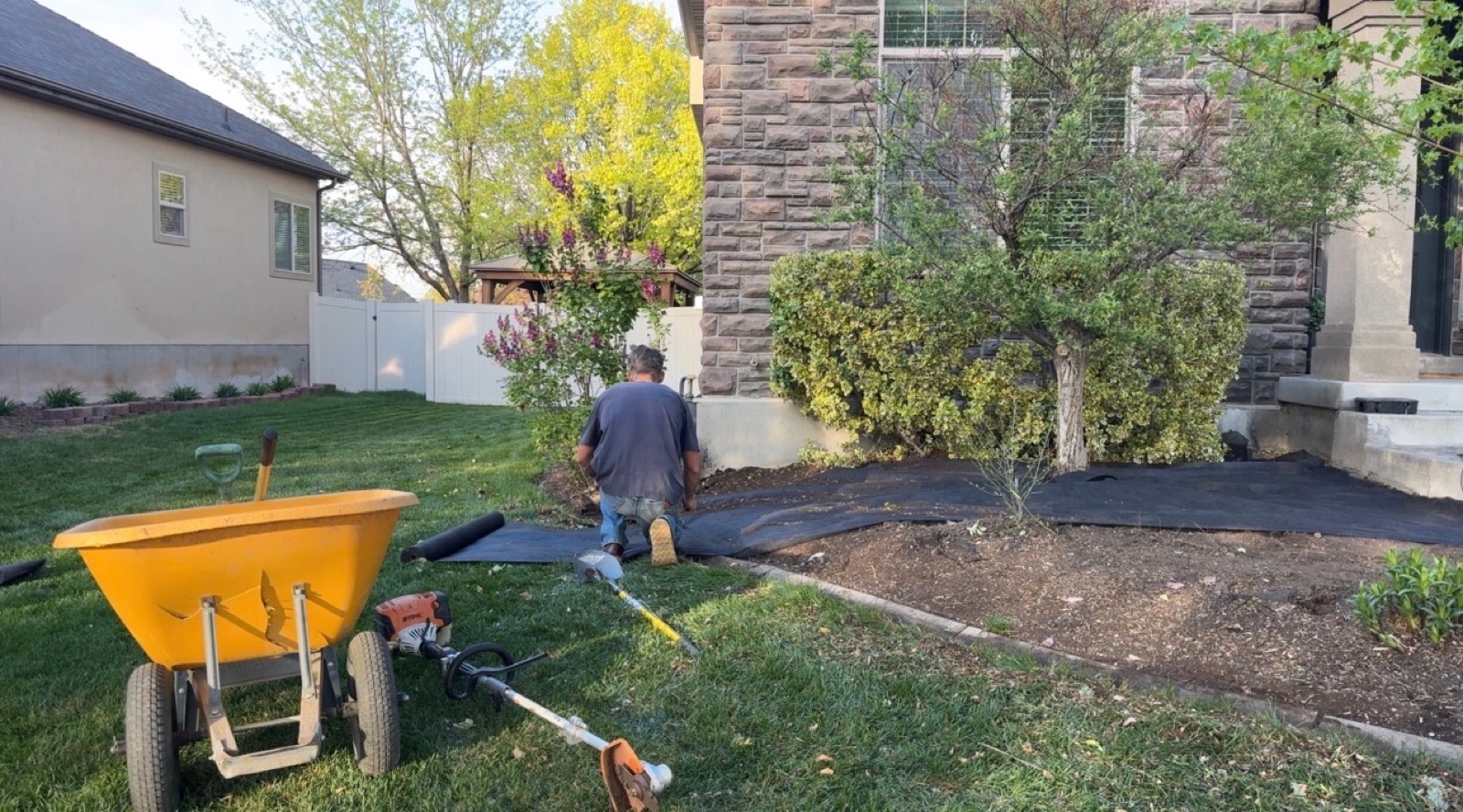 Crew member working in flower bed with wheelbarrow and tools